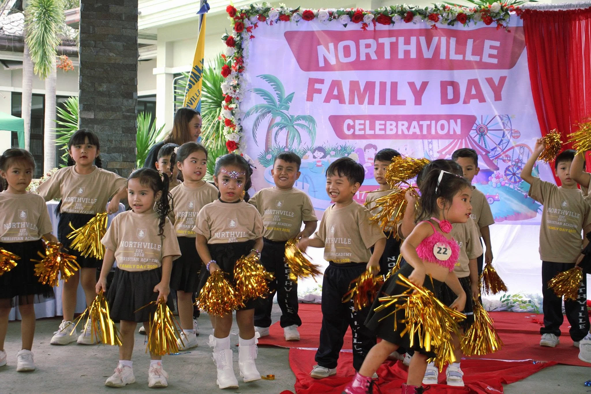Young children in gold performance outfits hold pom-poms at a Northville Family Day celebration.
